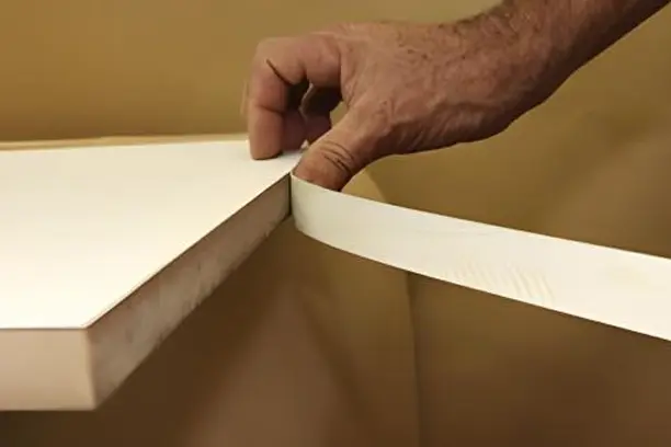Mão aplicando fita de borda numa peça de MDF
